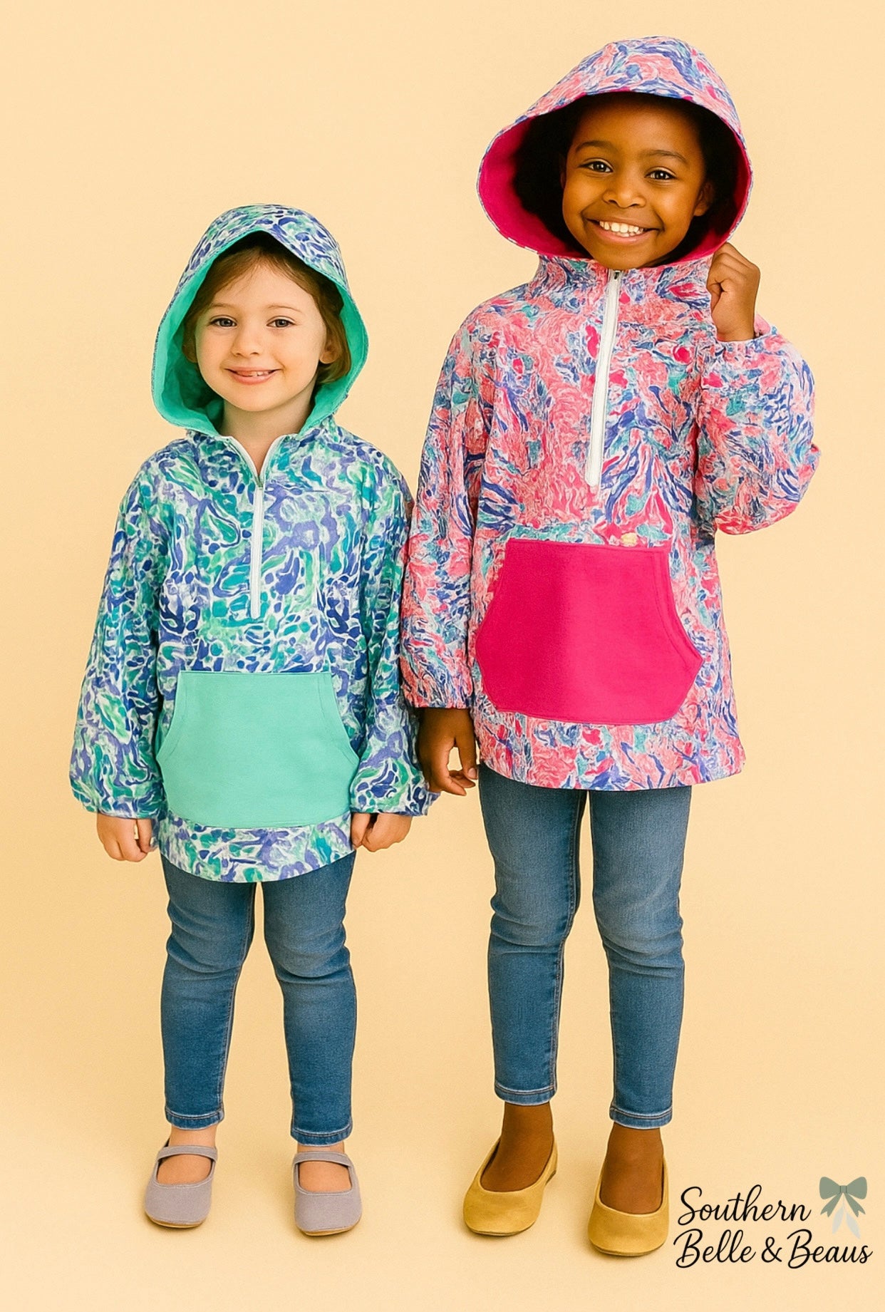 Two children wearing colorful hooded quarte-zips on a beige background