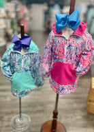 Two children's jackets with large bows on mannequins against a blurred indoor background.