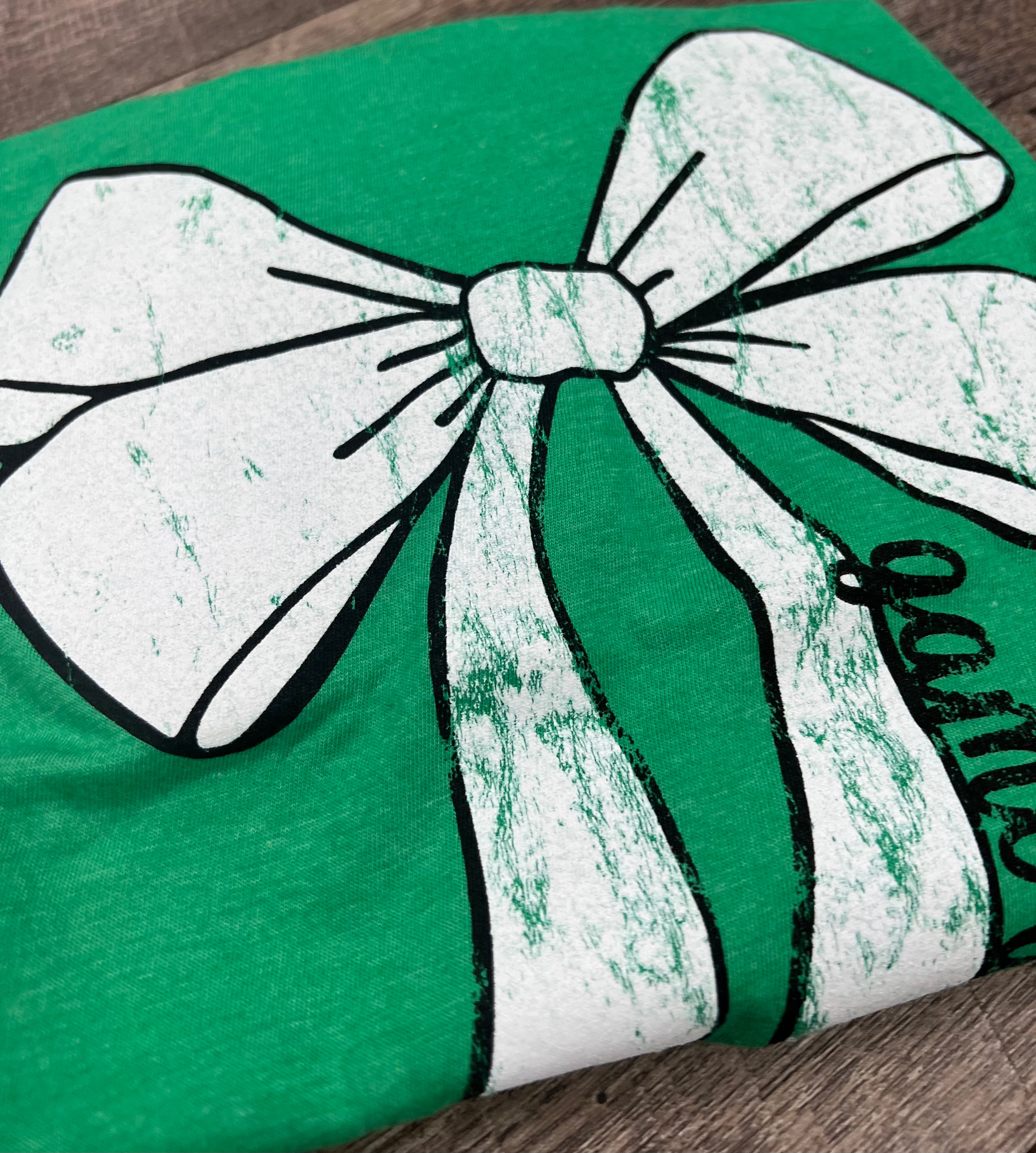 Green shirt with a large white bow design on a wooden surface