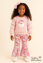 Young girl wearing a pink outfit with ruffled sleeves and patterned pants on a beige background.