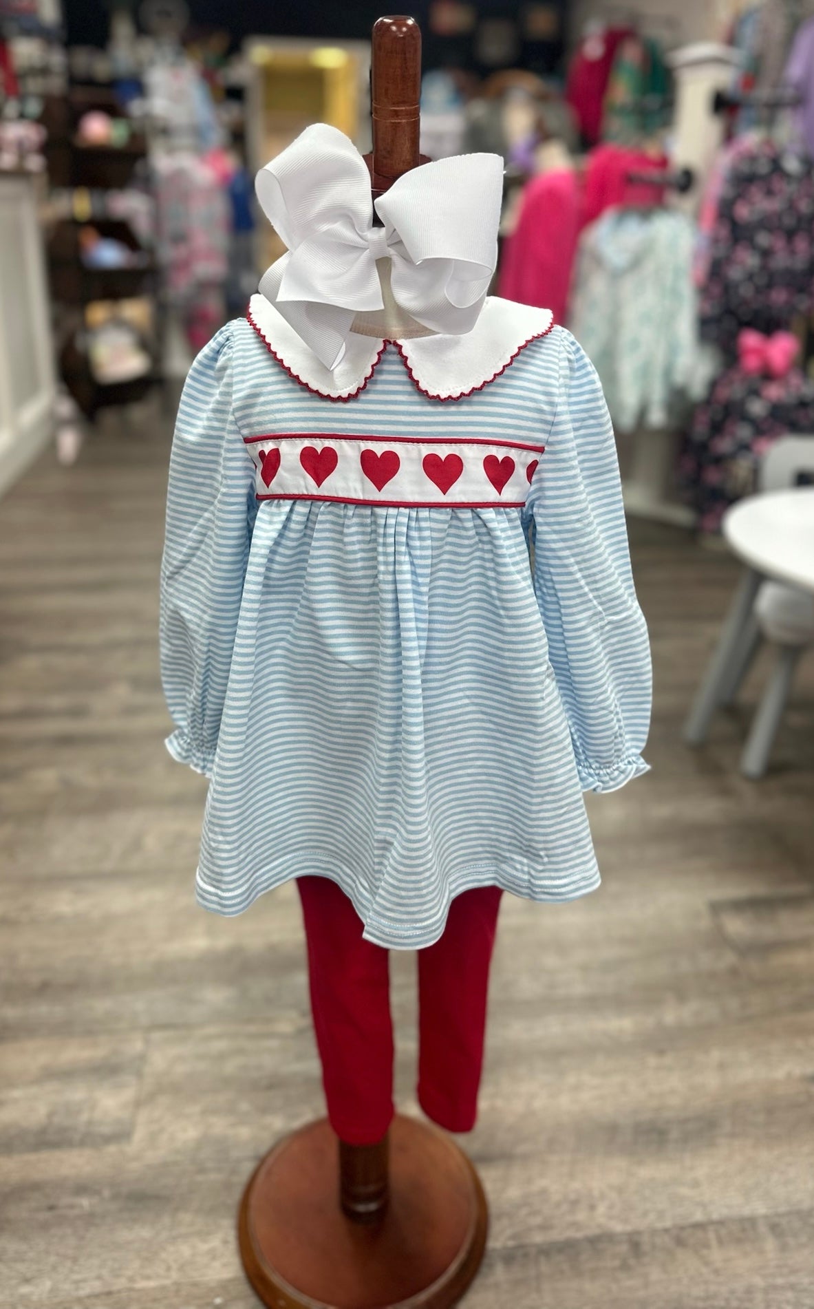 Girl’s dress with heart pattern and red pants on a mannequin in a store setting.