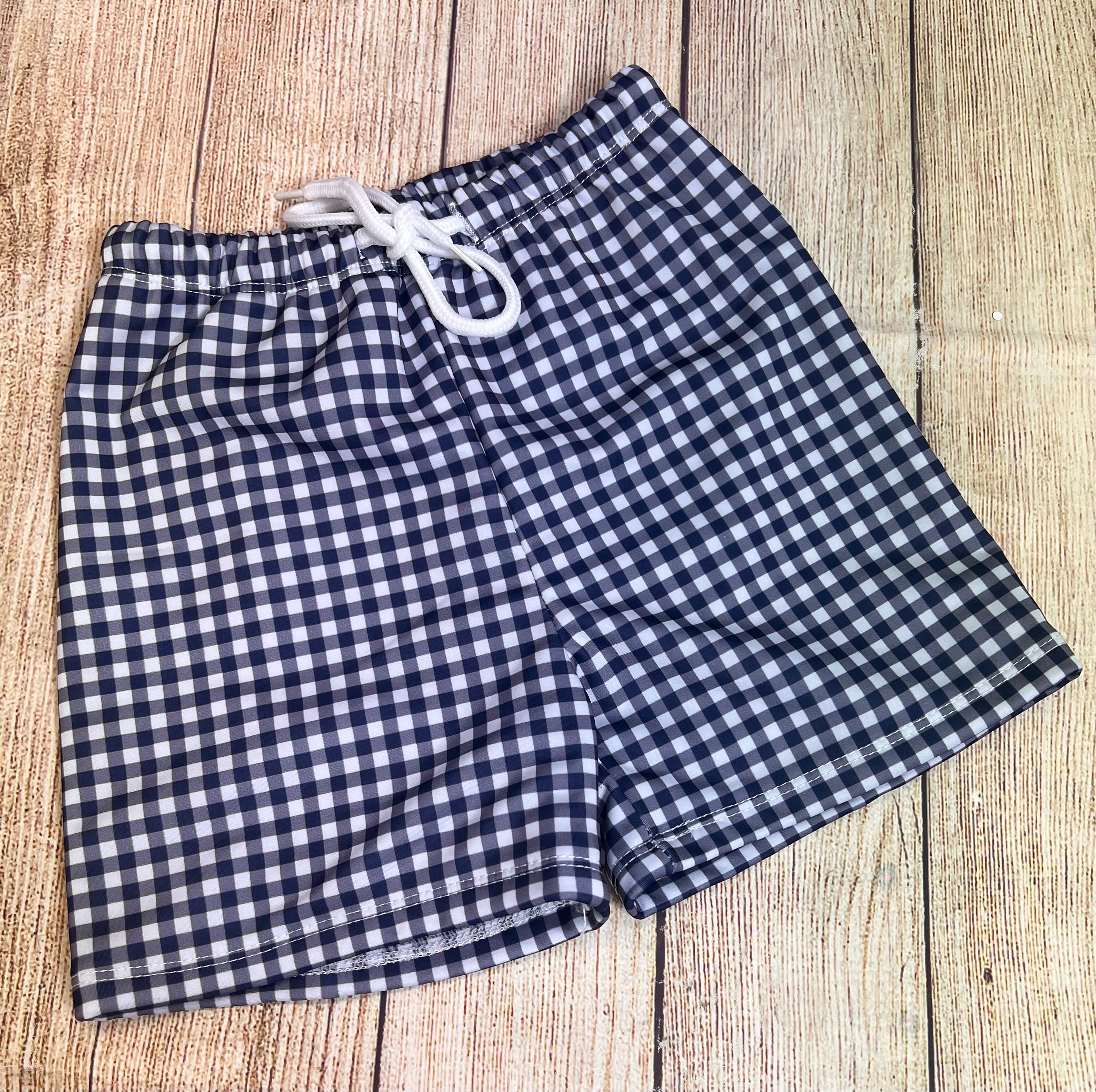 blue and white check boy swim trunks laying on a wood backdrop
