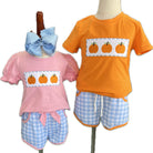 Two children's outfits on mannequins with pumpkin design shirts and checkered shorts.