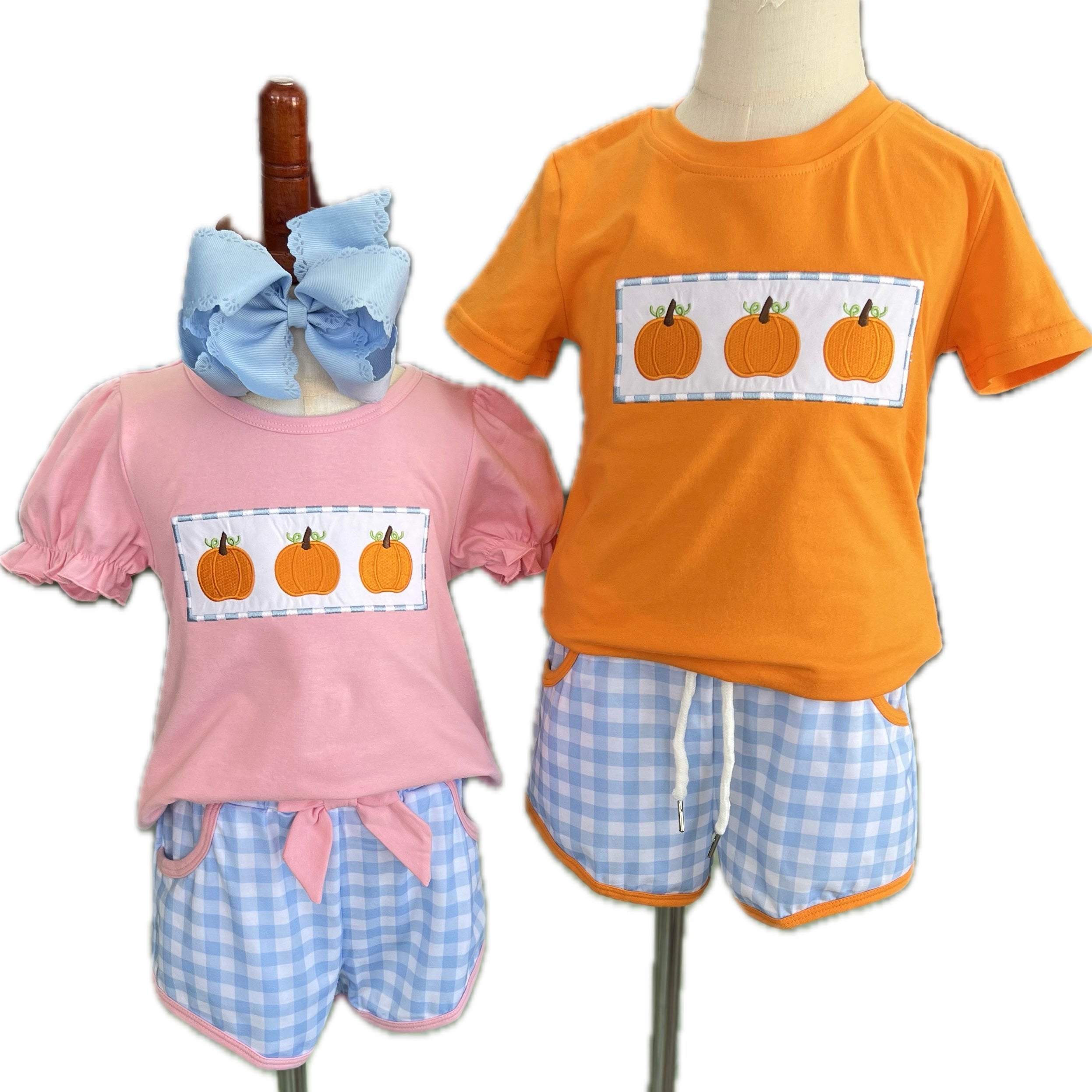 Two children's outfits on mannequins with pumpkin design shirts and checkered shorts.