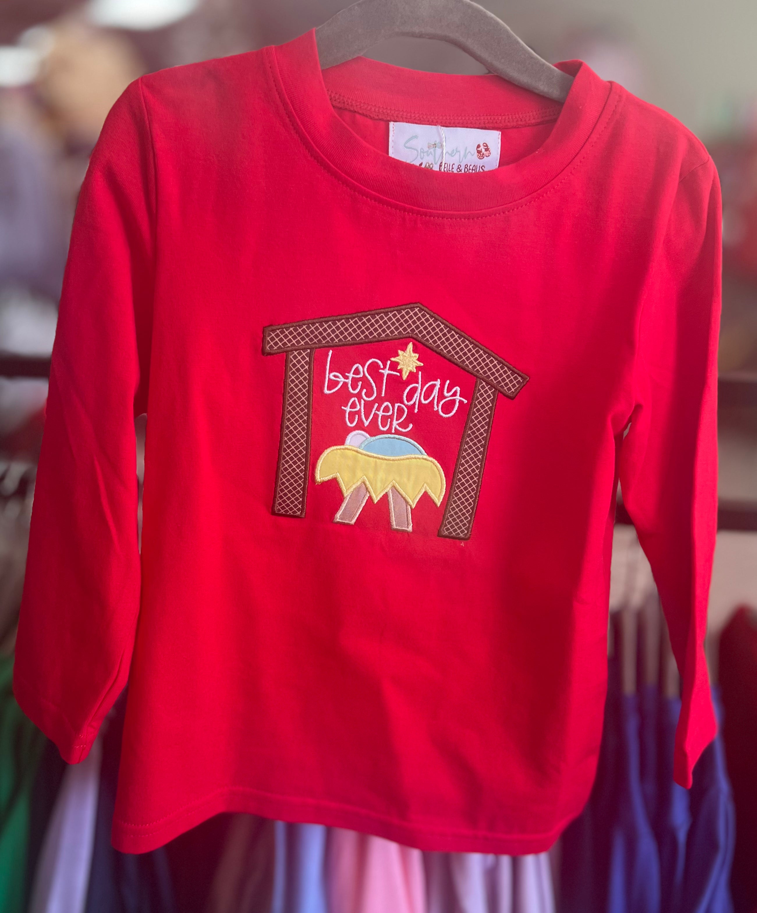 A red long-sleeved children's t-shirt with a Christmas-themed graphic of a manger scene and the text 'Best Day Ever' displayed on it.