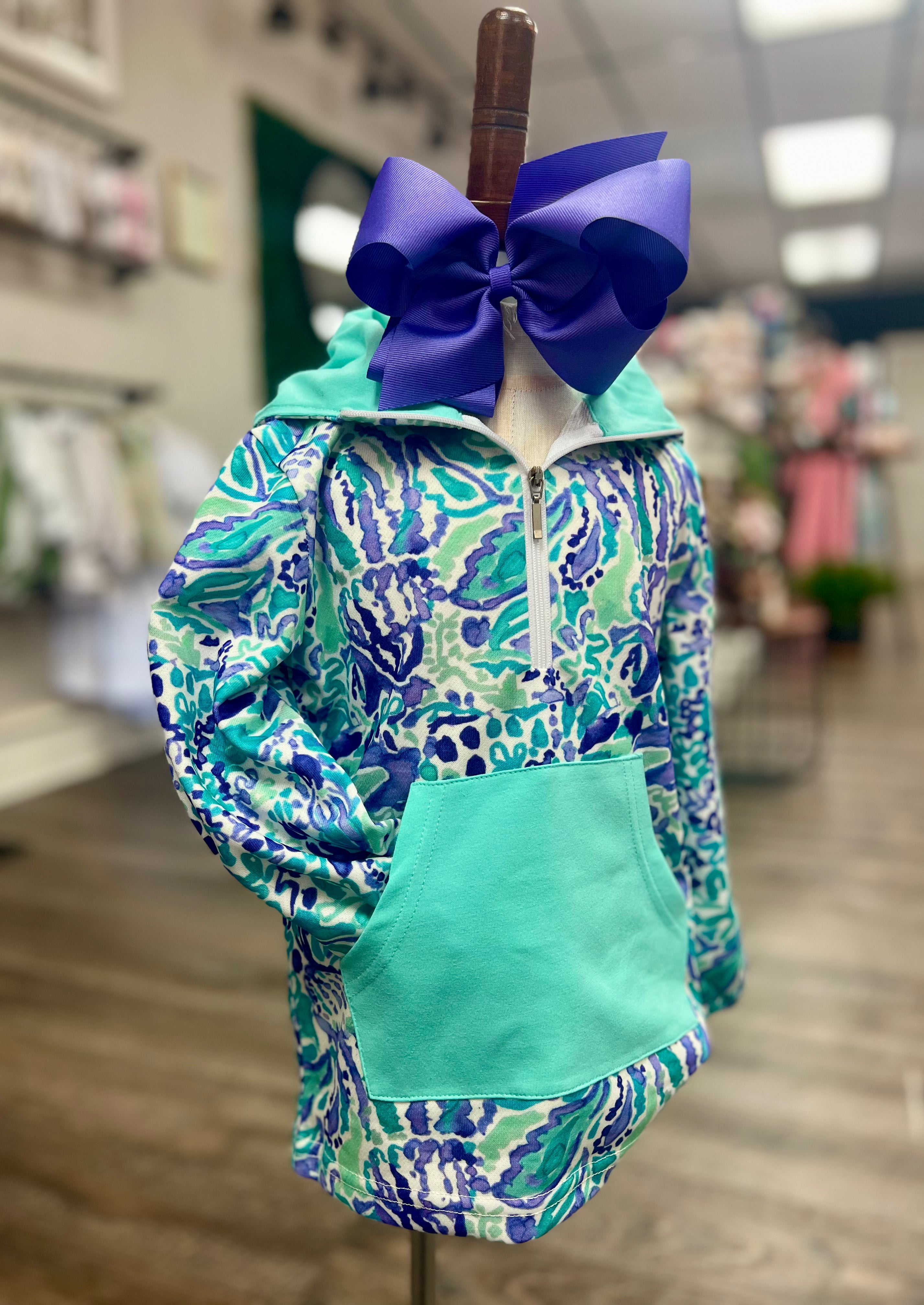 Teal and blue patterned jacket with a large purple bow on a mannequin in a store setting.