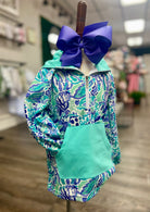 Teal and blue patterned jacket with a large purple bow on a mannequin in a store setting.