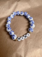 A bracelet with white and blue ceramic beads, and gold accents, spelling out 'GIGI'