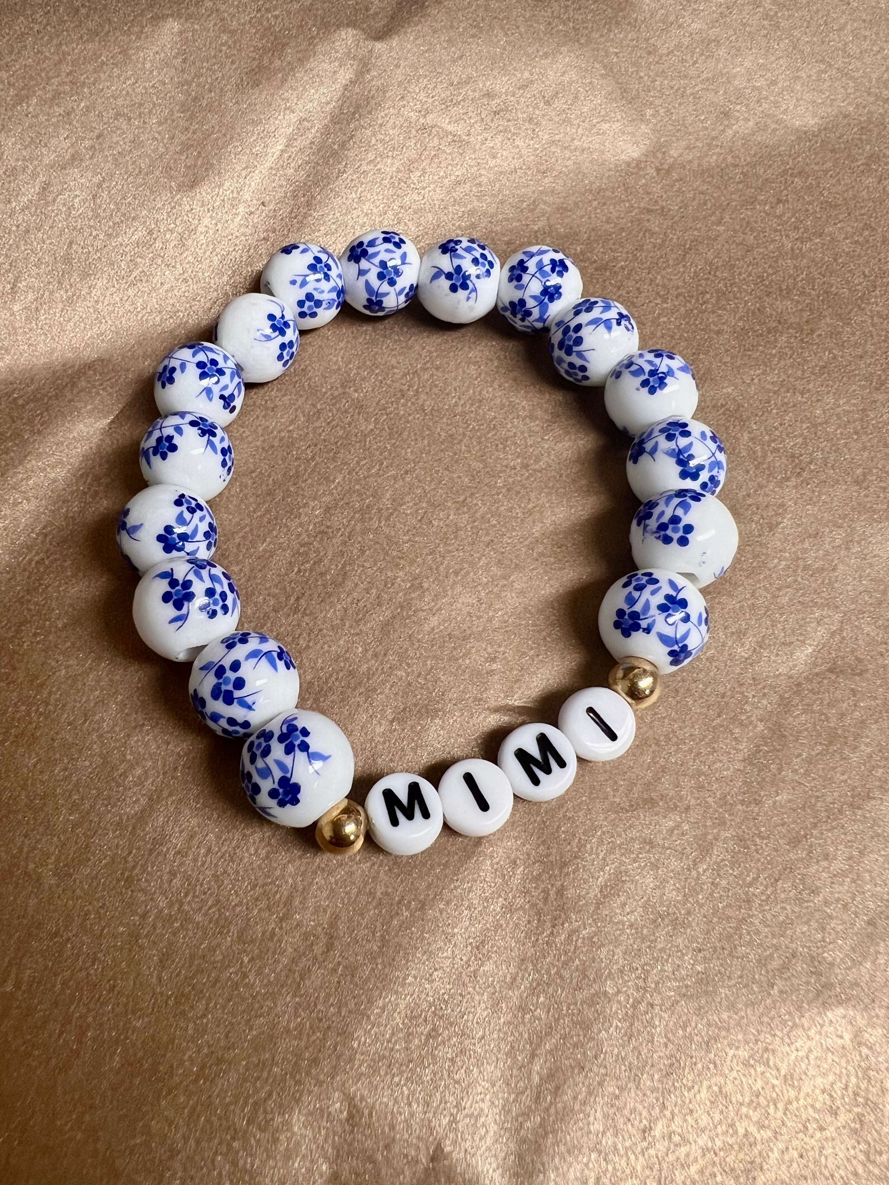 A bracelet with white and blue ceramic beads, and gold accents, spelling out 'GIGI'