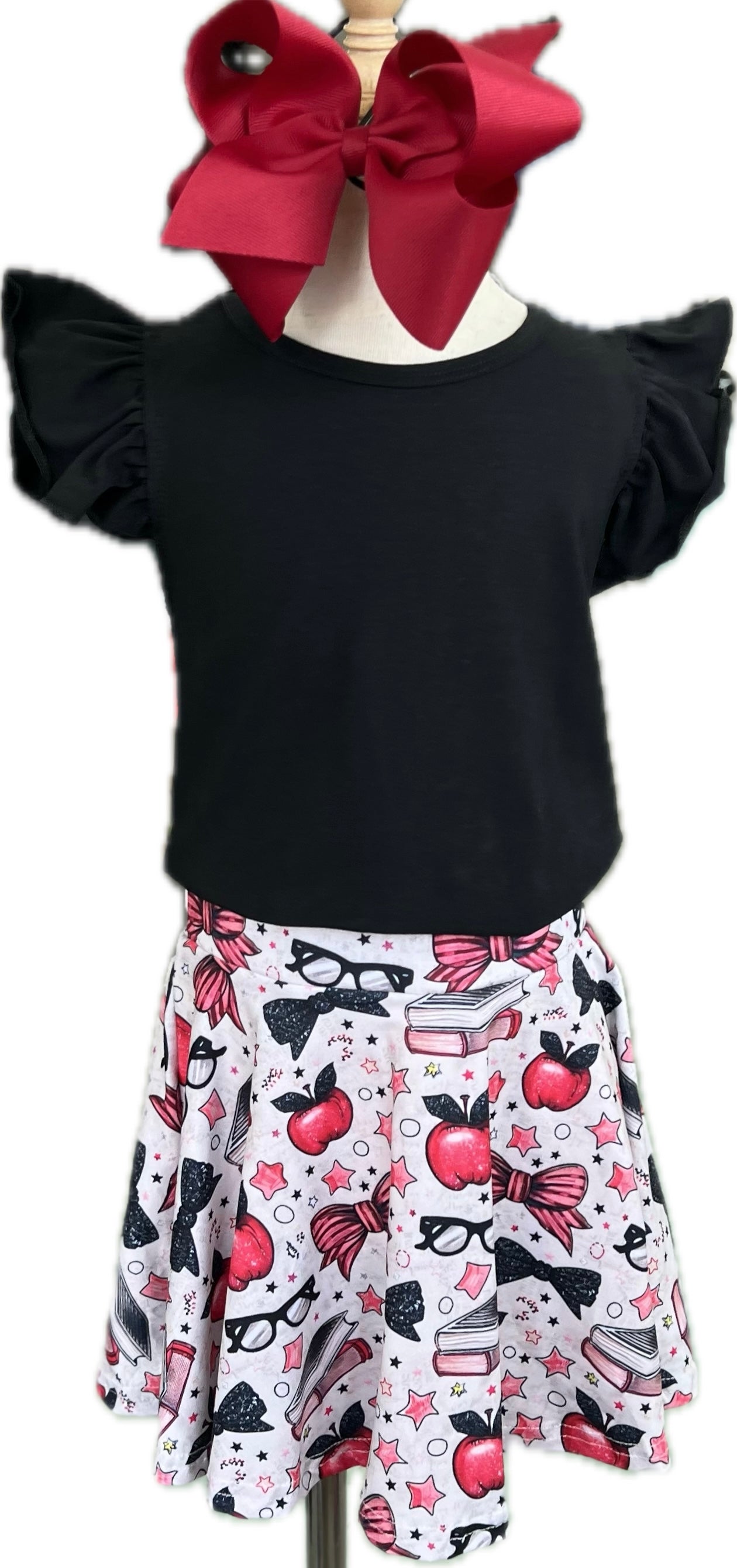 Black top with ruffled sleeves and a white skirt with red apples, black bows, and glasses on a mannequin.