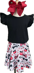 Black top with ruffled sleeves and a white skirt with red apples, black bows, and glasses on a mannequin.