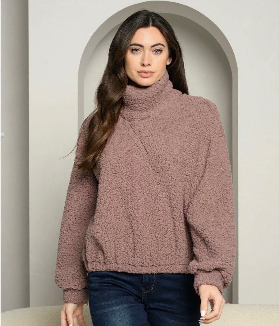 Woman wearing a brown turtleneck sweater and dark jeans in an archway.