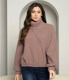 Woman wearing a brown turtleneck sweater and dark jeans in an archway.