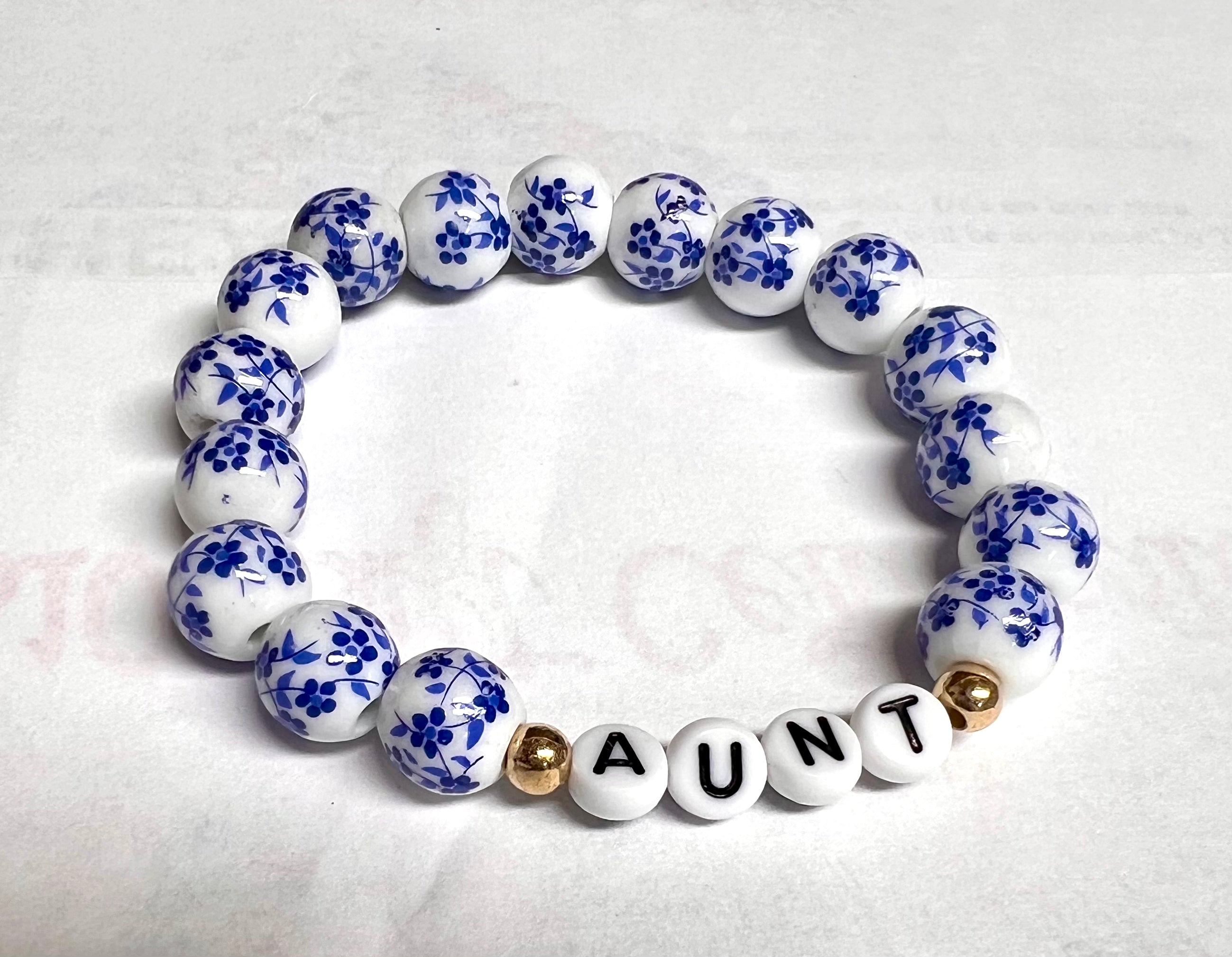 A bracelet with white and blue ceramic beads, and gold accents, spelling out 'GIGI'