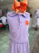 Purple dress with orange bow and paw print on a mannequin against a blurred indoor background