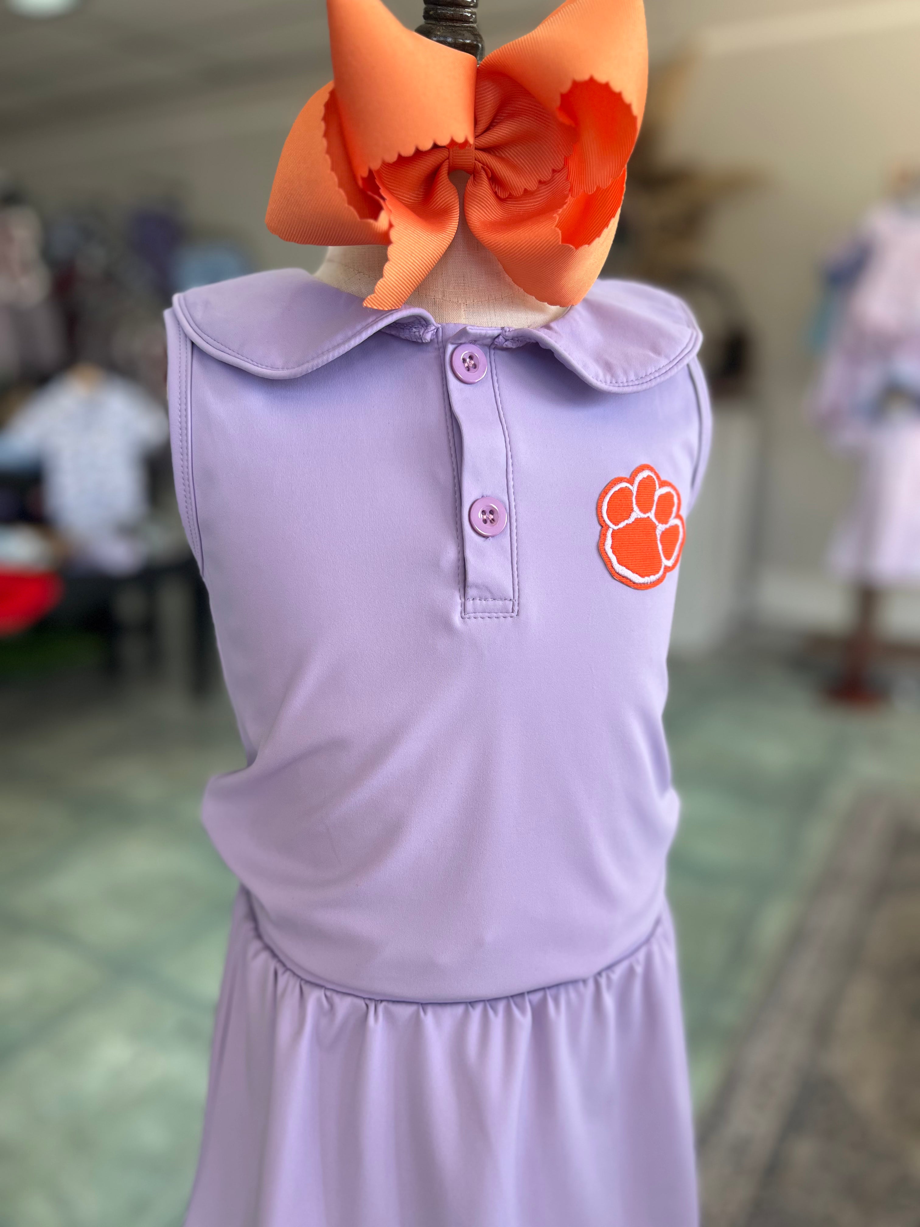 Purple dress with orange bow and paw print on a mannequin against a blurred indoor background