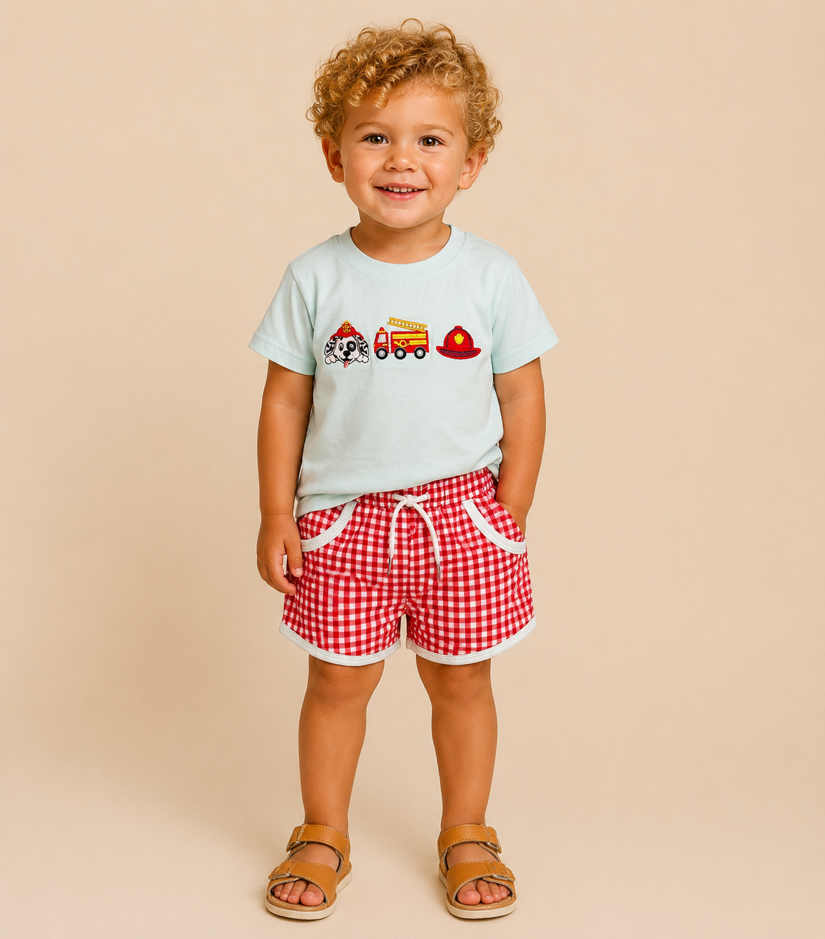 Toddler boy wearing a fire fighter themed shirt with red checkered shorts.