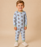 A young child wearing a light blue and white checkered long-sleeve pajama set with astronaut print , standing against a solid beige background.