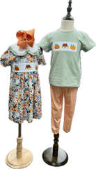 Children's floral dress and green t-shirt with pumpkin design on mannequins against a white background.