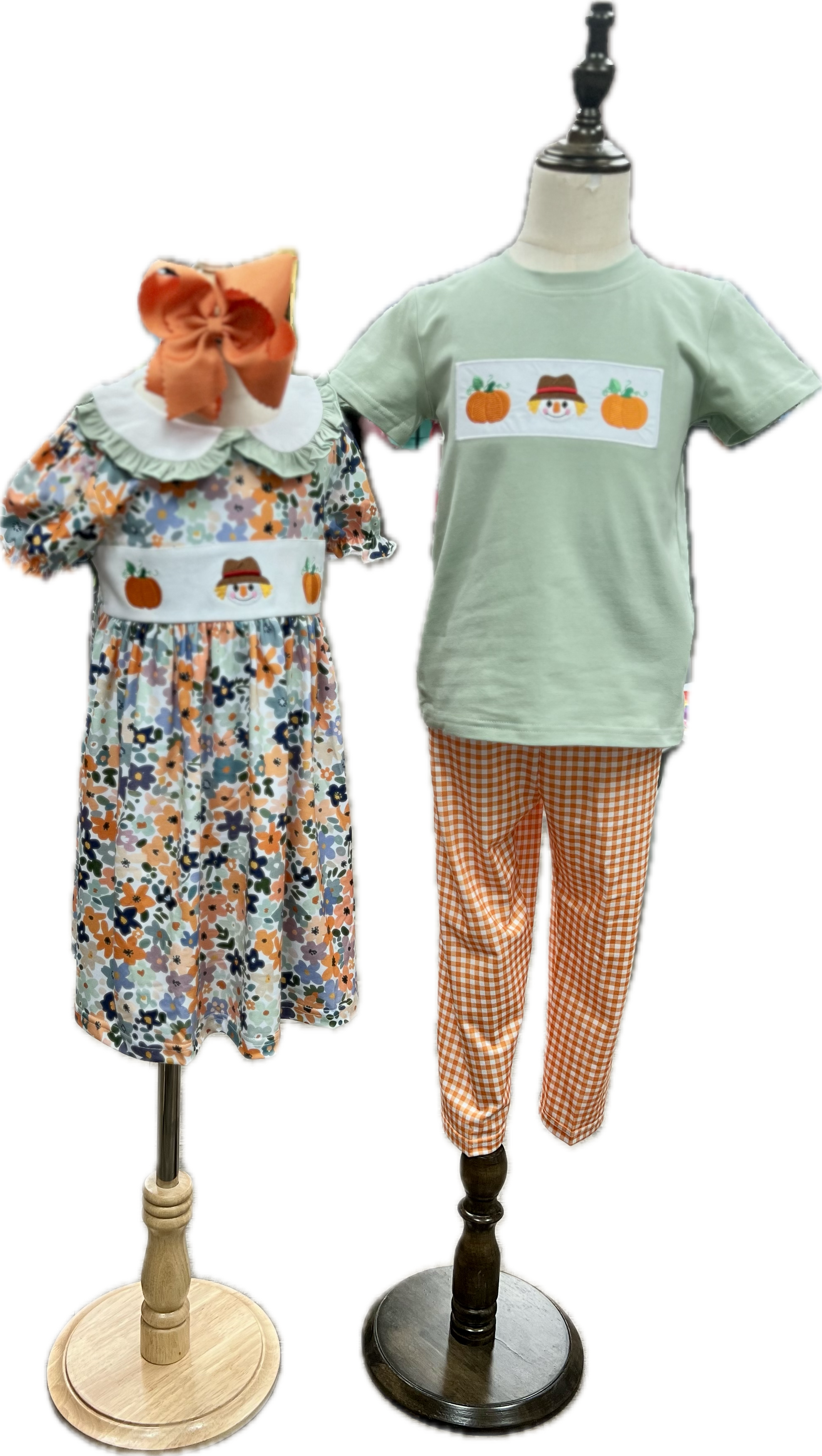 Children's floral dress and green t-shirt with pumpkin design on mannequins against a white background.