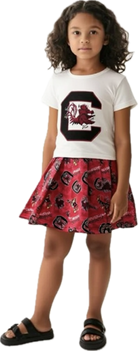 Young girl wearing a white t-shirt with a logo and a red skirt with a similar logo design.