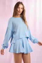 Woman wearing a light blue outfit with a matching top and skirt on a pink background