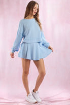Woman wearing a light blue outfit with a skirt on a pink background
