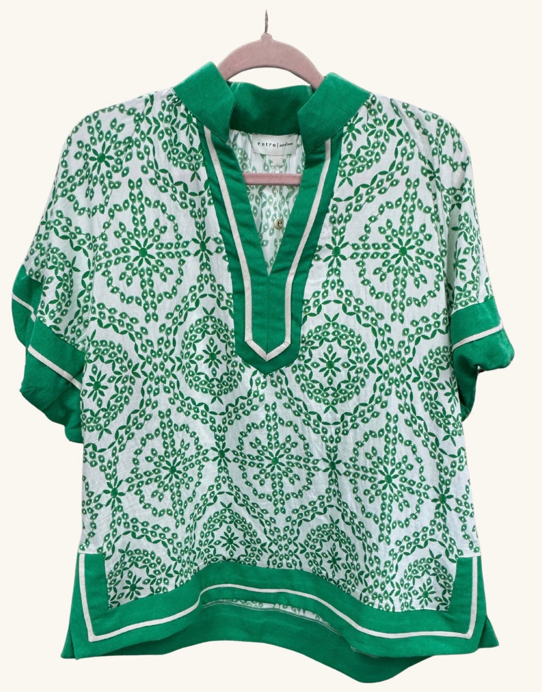 Green and white geometric patterned top with split neckline, contrast trim, and short sleeves, featuring a relaxed fit and lightweight fabric.