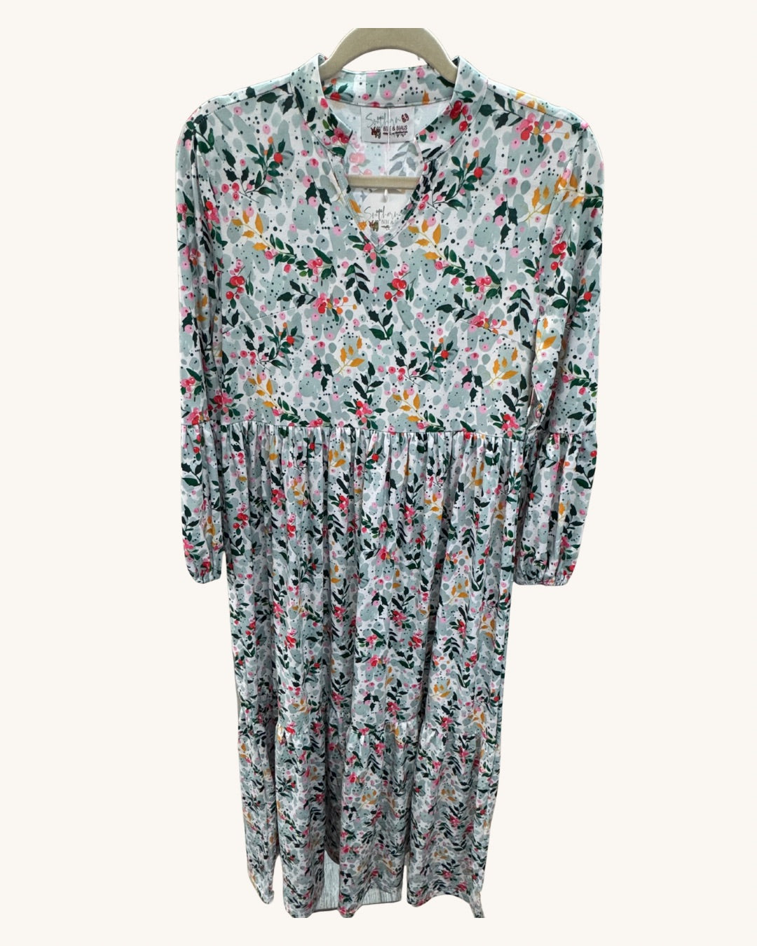 Long floral dress with a light background featuring pink, yellow, and green botanical print, V-neckline, long sleeves, and gathered waist detail.