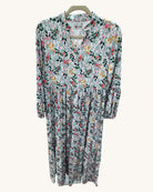 Long floral dress with a light background featuring pink, yellow, and green botanical print, V-neckline, long sleeves, and gathered waist detail.