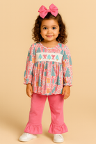 Child wearing a colorful top and pink pants with a bow on a beige background