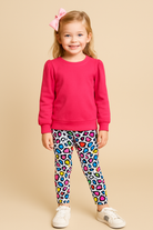 Child wearing a pink sweatshirt and colorful leopard print leggings on a beige background