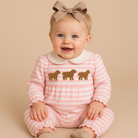 Baby wearing a pink and white striped outfit with gold sheep designs on a beige background