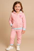 Young girl wearing a pink hooded jogger with a bow detail on a beige background
