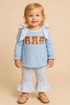 Child wearing a light blue top with teddy bear designs and checkered pants on a beige background