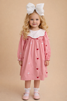 Young girl wearing a pink dress with heart patterns and a white bow headband on a beige background