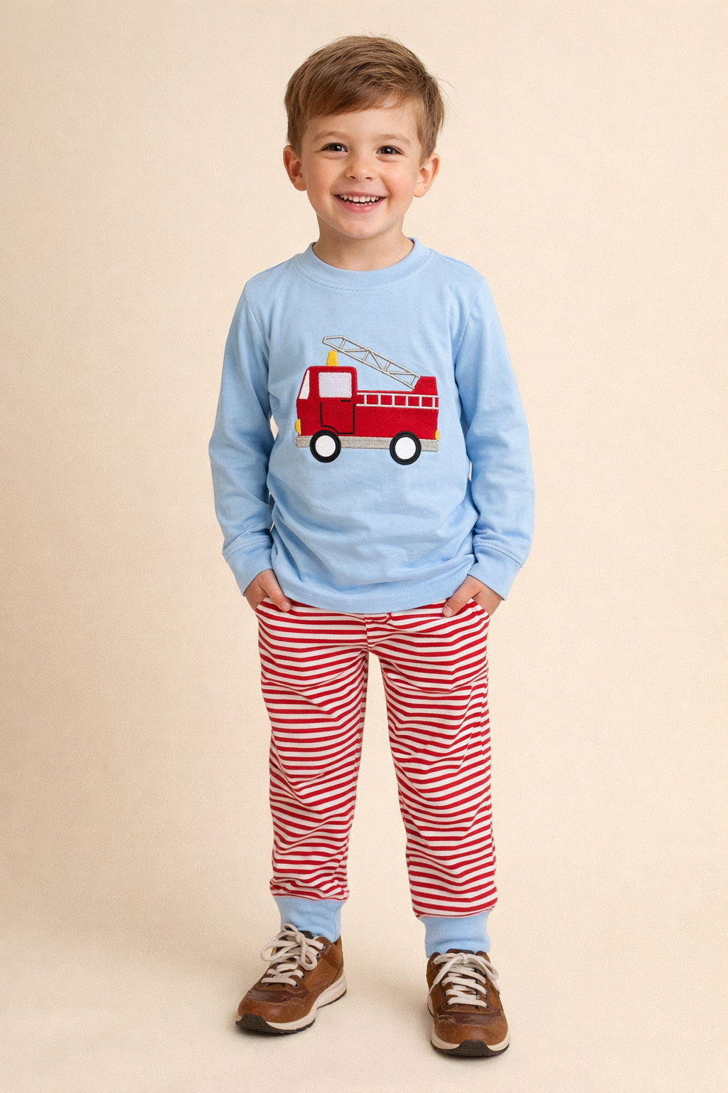Child wearing a blue shirt with a red fire truck graphic and red striped pants on a beige background