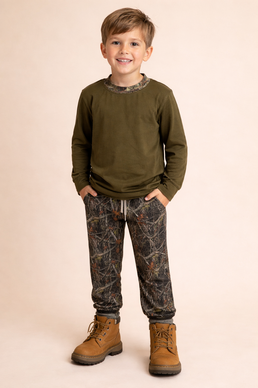 A boy wearing a dark green shirt with camo joggers and boots.