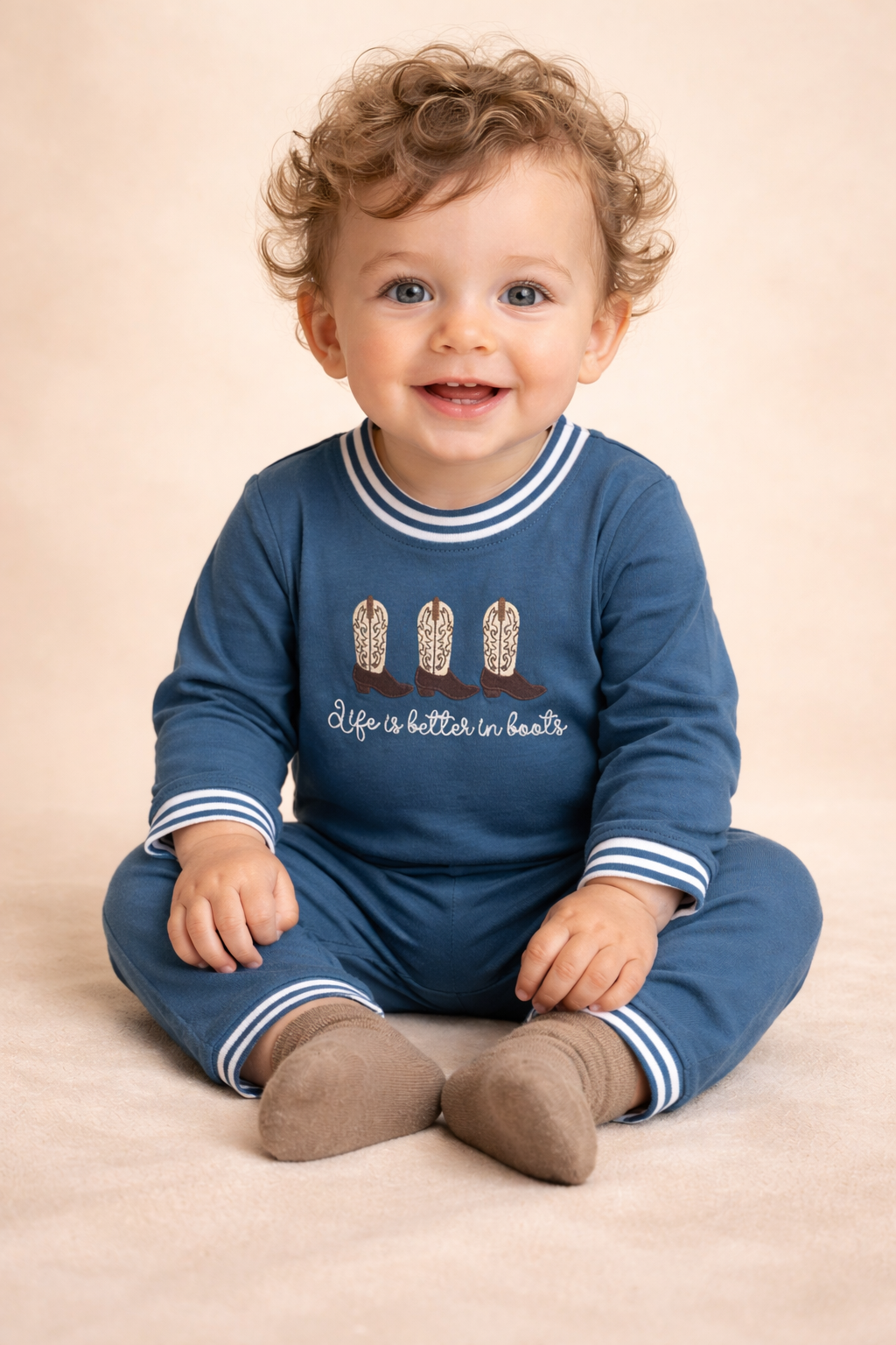 Baby boy wearing a dusty blue romper that has boots on the chest area. 