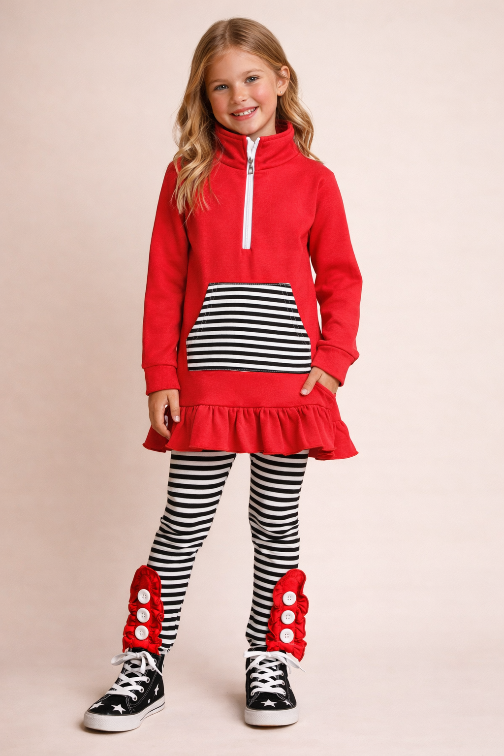 Young girl wearing a red zip pullover with black and white striped leggings and shoes on a beige background