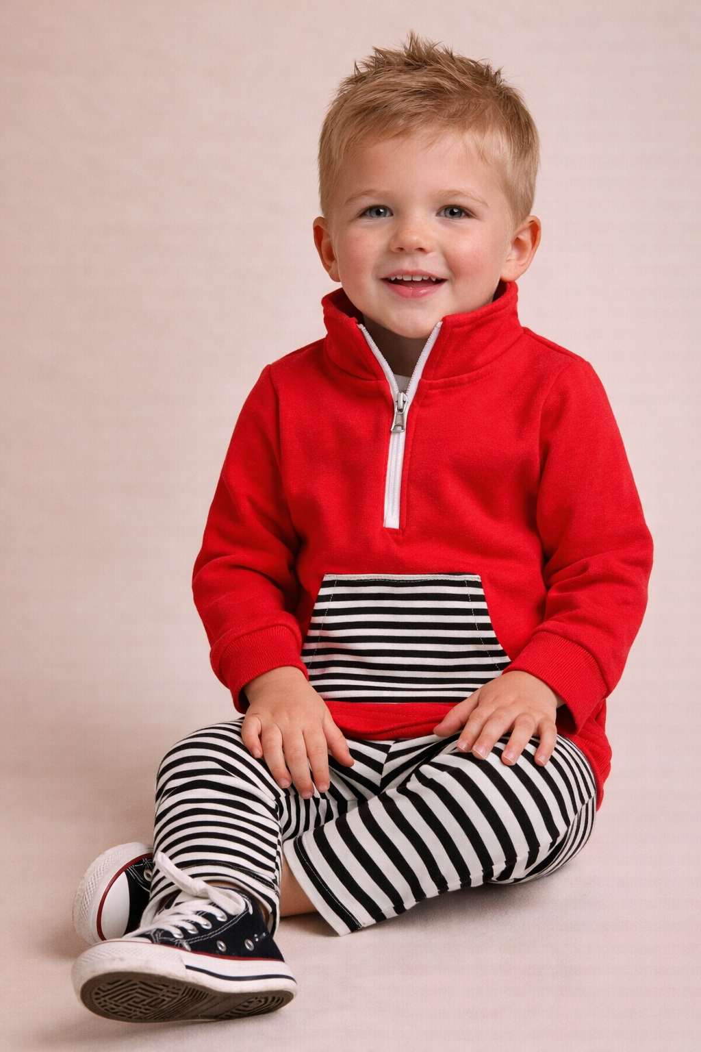 Child wearing a red  pullover with a striped black and white outfit on a beige background