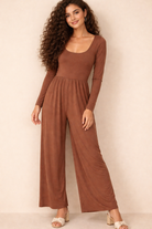 Lady wearing a long sleeve brown jumpsuit on beige background. 