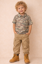 Little boy with a washed camo polo with khaki cargo pants and boots. 