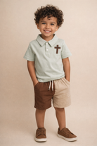 Curly haired boy with sage green cross polo with shorts.