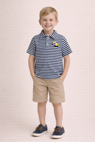 Young boy wearing a striped polo shirt and shorts on a light pink background