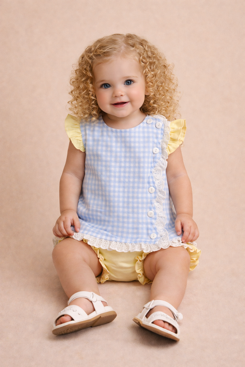 Baby girl wearing a blue gingham top with yellow accents.