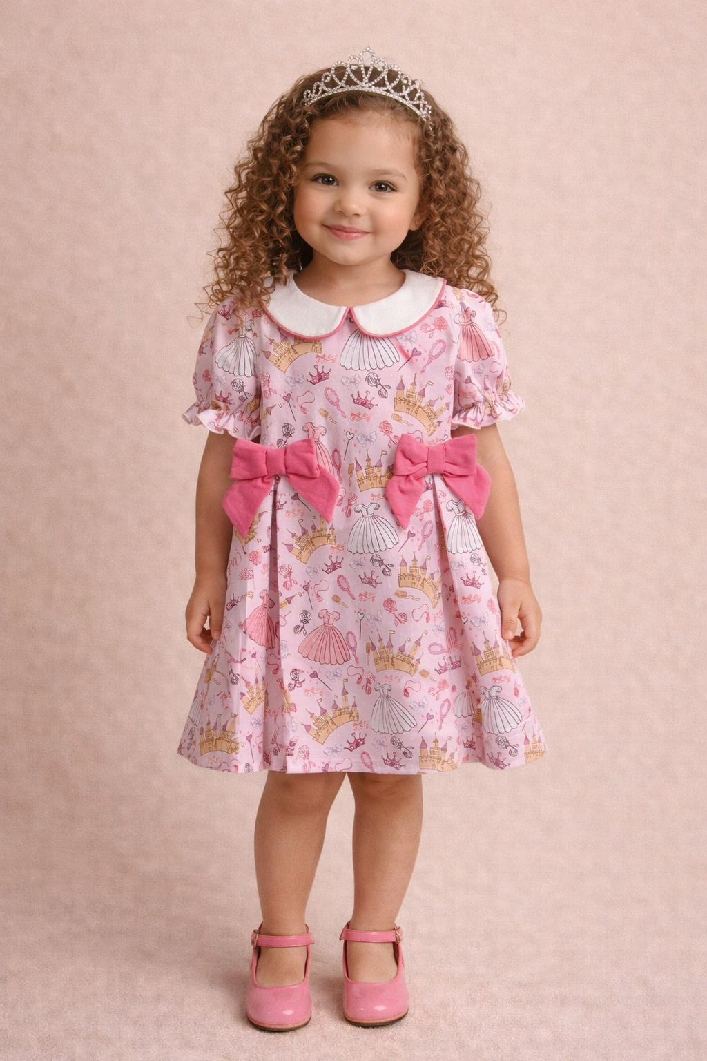 Young child wearing a pink dress with pink shoes and a tiara. 