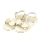 Pair of champagne-colored sandals with bow details on a white background