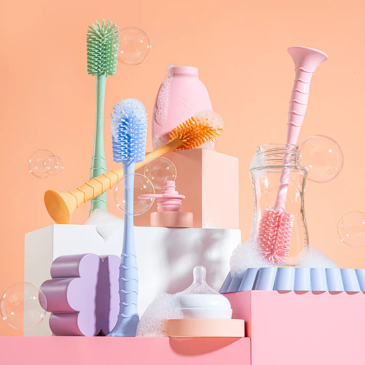 Collection of colorful baby bottle cleaning brushes and tools on a pink background