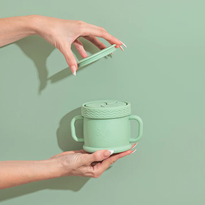 Person holding a mint green mug with a lid against a light green background